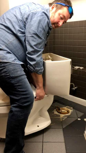 How to know if your toilet seal is leaking. Image shows plumber removing a toilet to locate a leaky wax toilet ring.